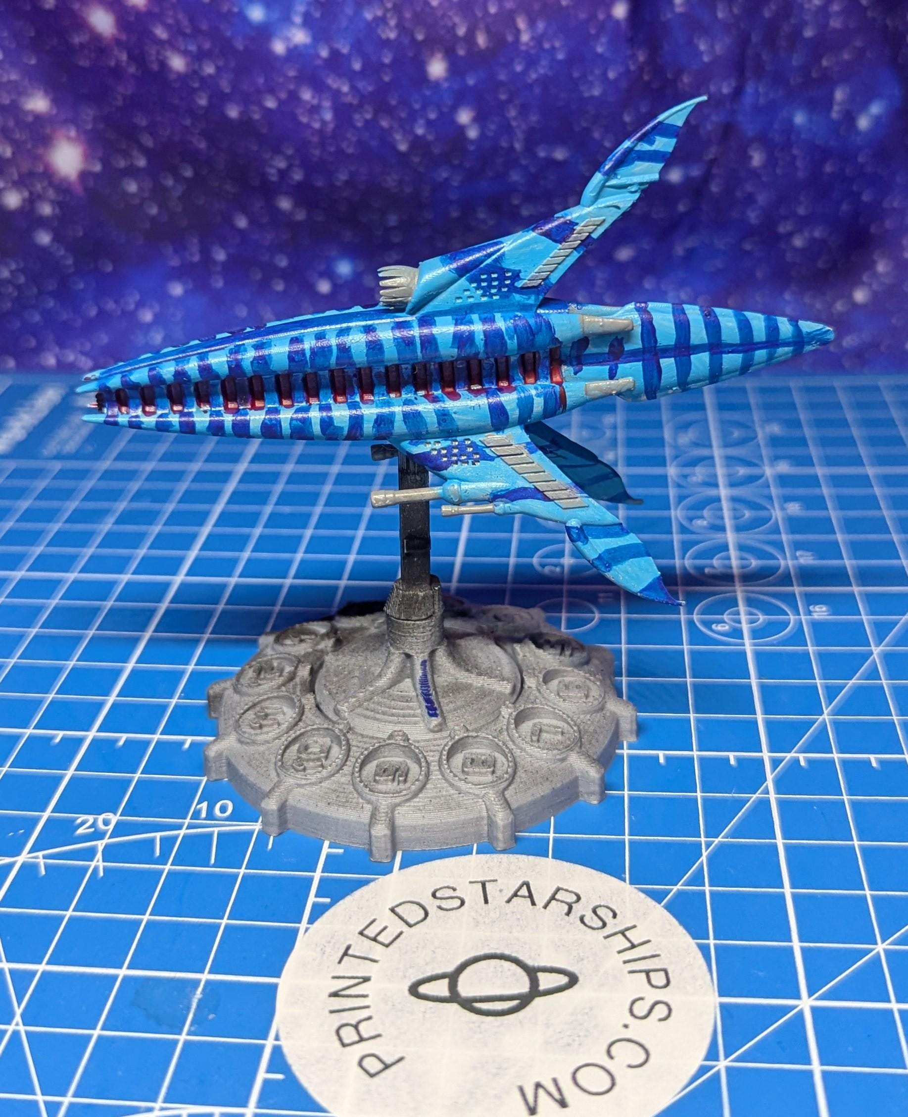 May include: A blue and red striped spaceship with gray wings and a gray base. The base has a circular design with multiple circles around the edge. The base is labeled 'PRINTEDSTARSHIPS.COM'.