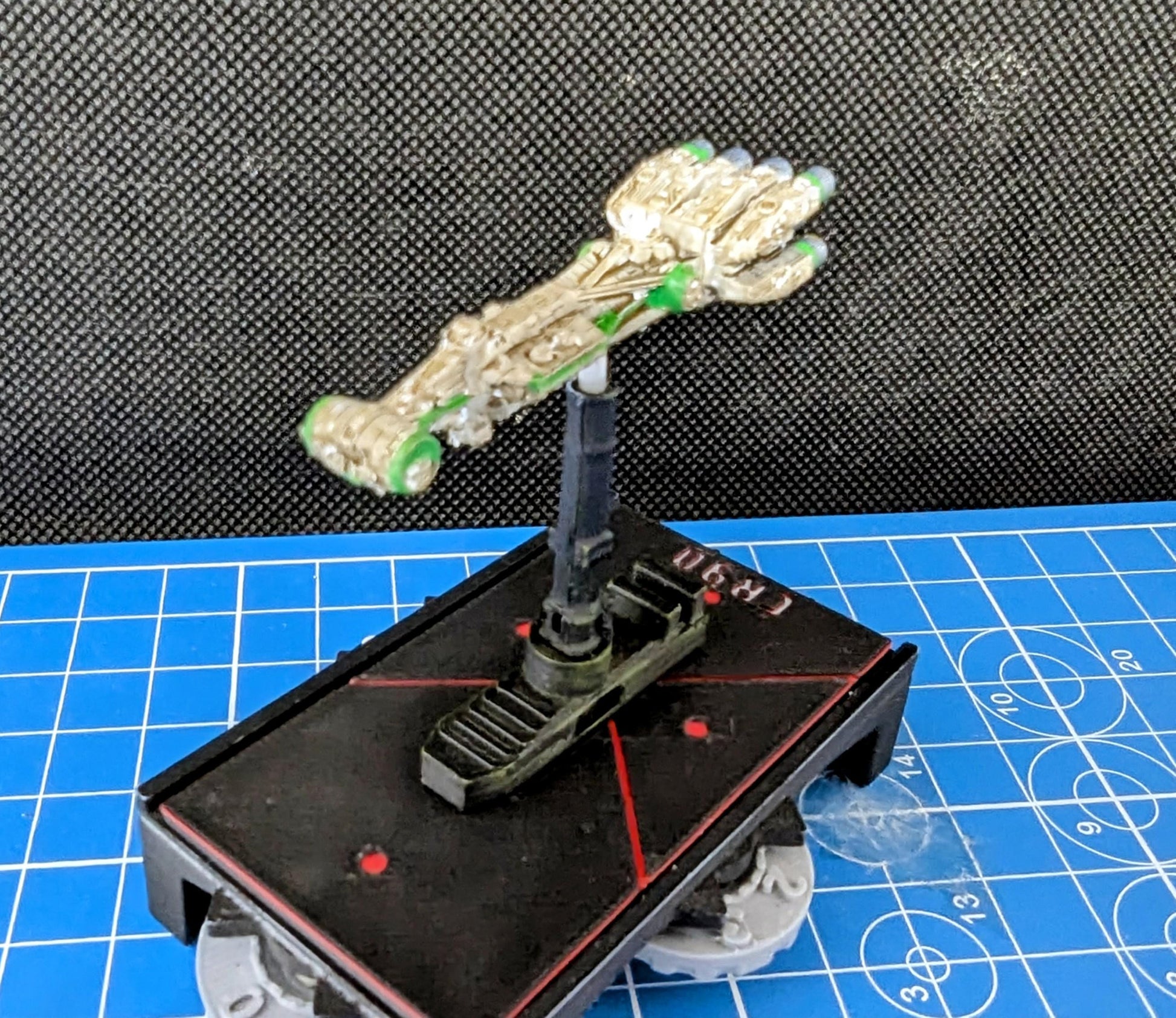 May include: A white and green plastic miniature hand attached to a black plastic base. The base is attached to a black plastic platform with a red line and the text 'CR30' printed on it.