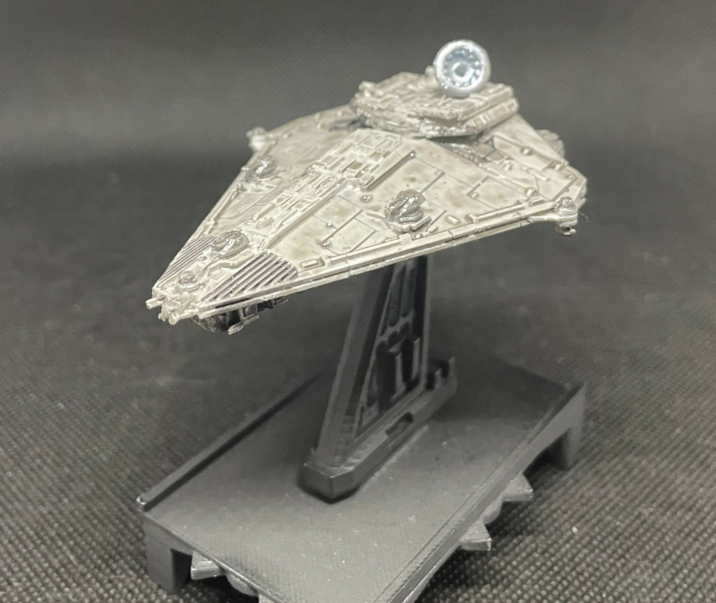 May include: A gray and silver spaceship model with a round, silver dome on top. The spaceship is on a black stand with a textured surface.
