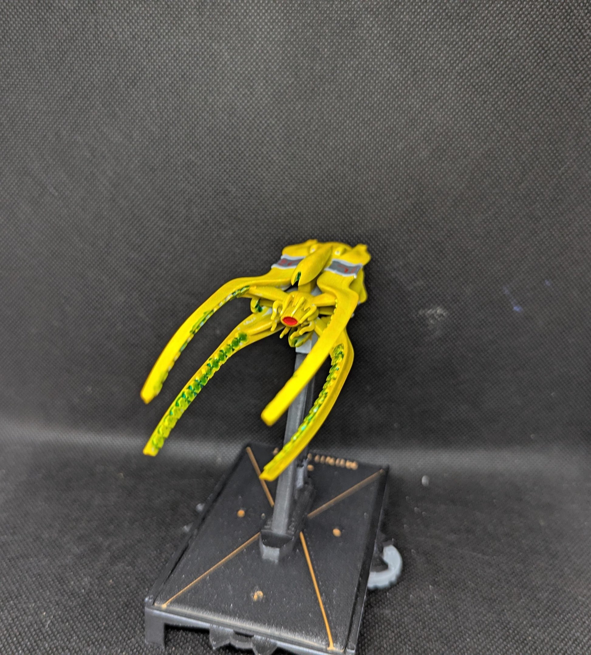 May include: A yellow spaceship with green details and a red eye. The spaceship is on a black stand with a gold trim.
