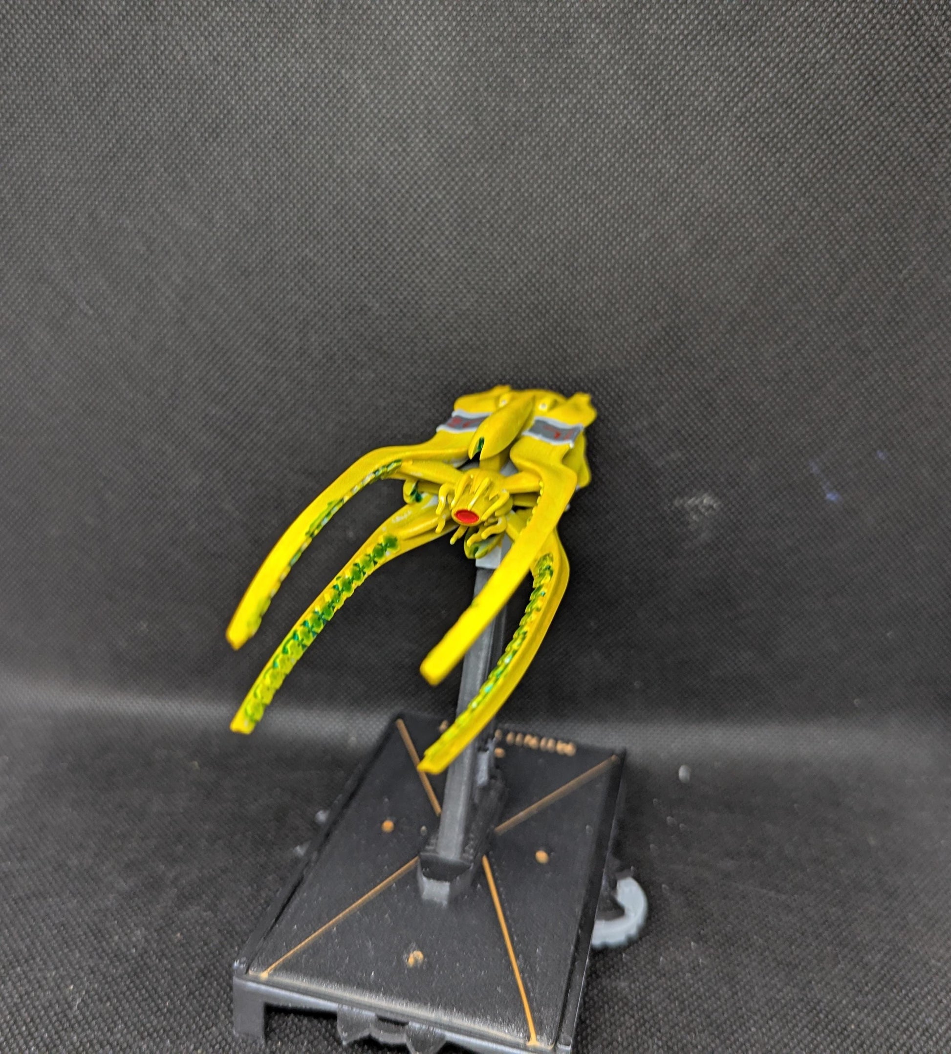 May include: A yellow spaceship with green details and a red eye. The spaceship is on a black stand with a gold trim.