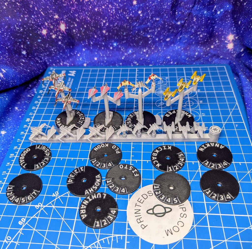 May include: A set of 10 black plastic circular tokens with white text. The text on the tokens includes the names 'Anakin', 'Zckback', 'Per', 'Se', 'Sto', 'PLO', 'Koon', 'Ahsoka', 'Lumi', and 'Oddball'. The tokens are arranged on a blue surface with a white sticker that says 'PRINTEDS IPS.COM'.