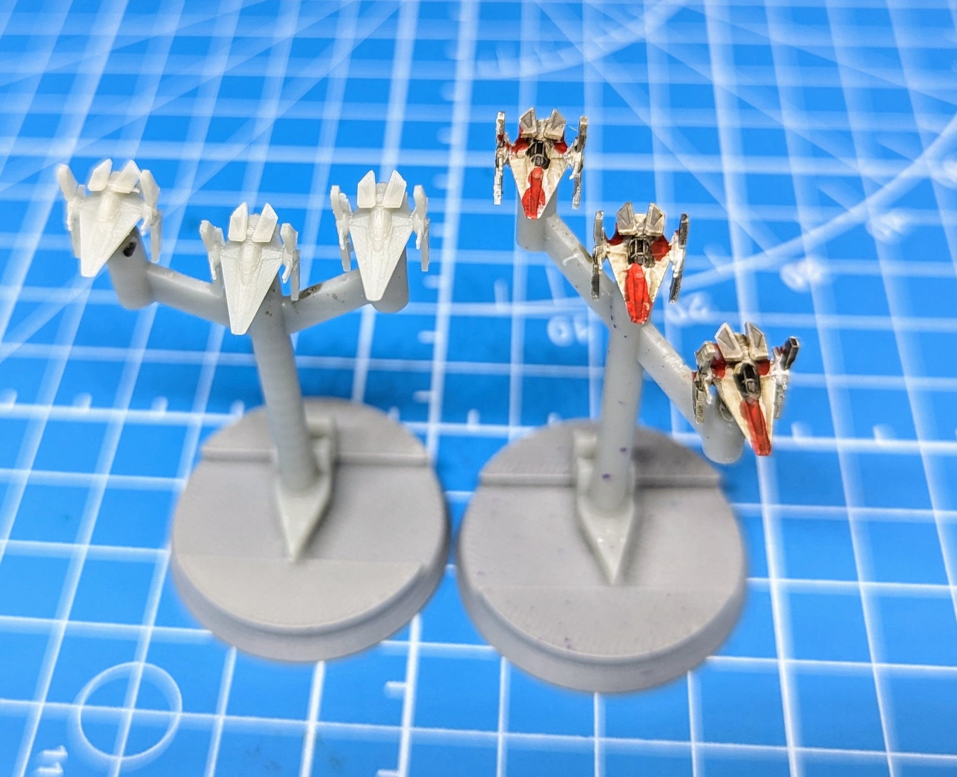 May include: Two sets of miniature X-wing starfighters on display stands. The starfighters are painted white with red accents. The stands are gray and circular. The starfighters are arranged in a symmetrical pattern on the stands.