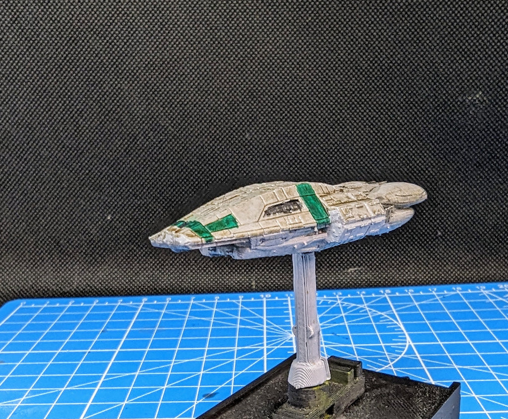 May include: A white and green spaceship model with a green stripe on the top. The model is on a white stand and a black base.