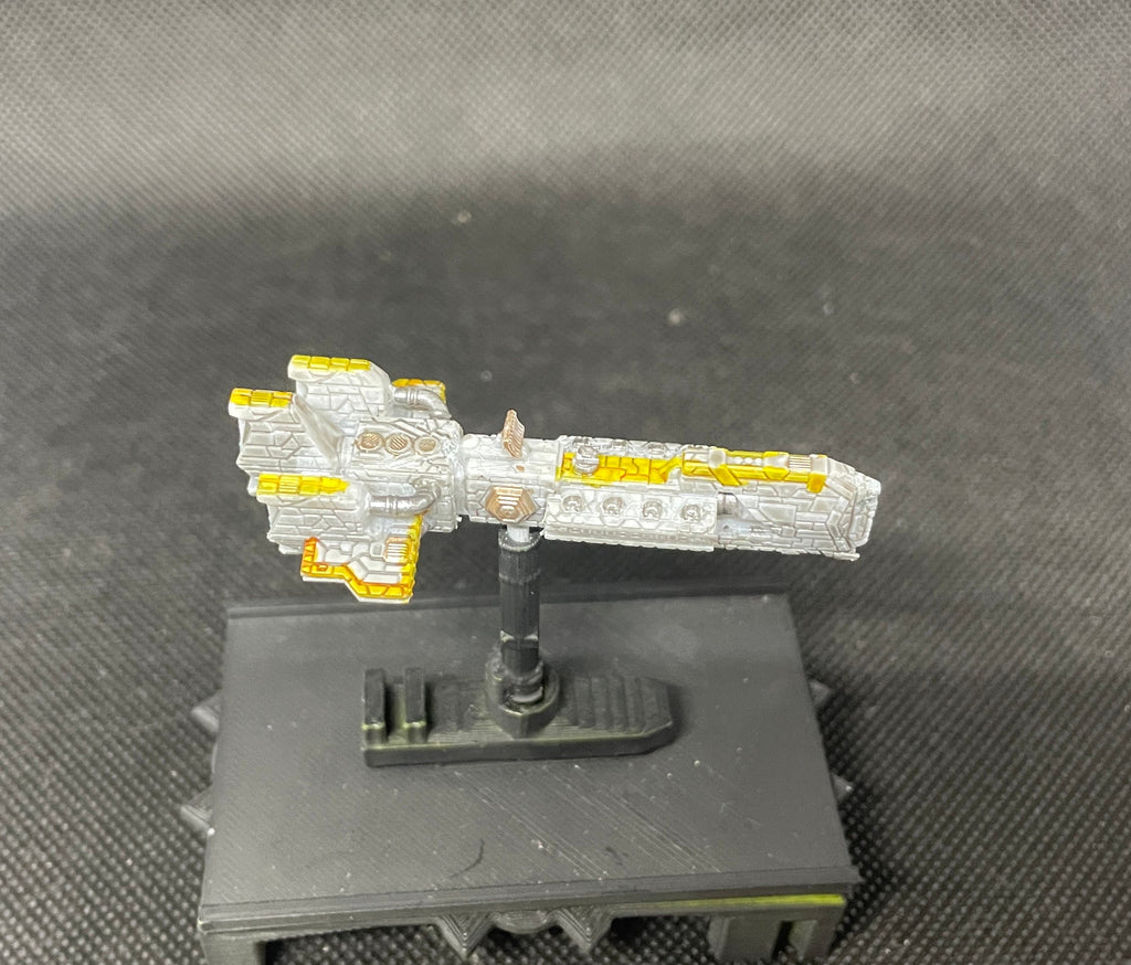 May include: A white and yellow spaceship model on a black base. The spaceship has a detailed design with a pointed nose and a long, thin body. The spaceship is painted in a silver and gold color scheme.