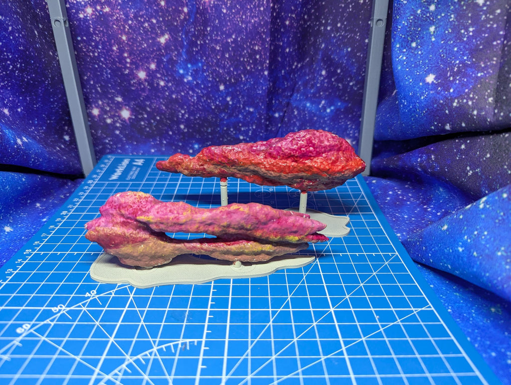 May include: Two pink and red rock formations on a blue grid surface. The rocks are painted with a variety of colors and textures. The rocks are on a white base.