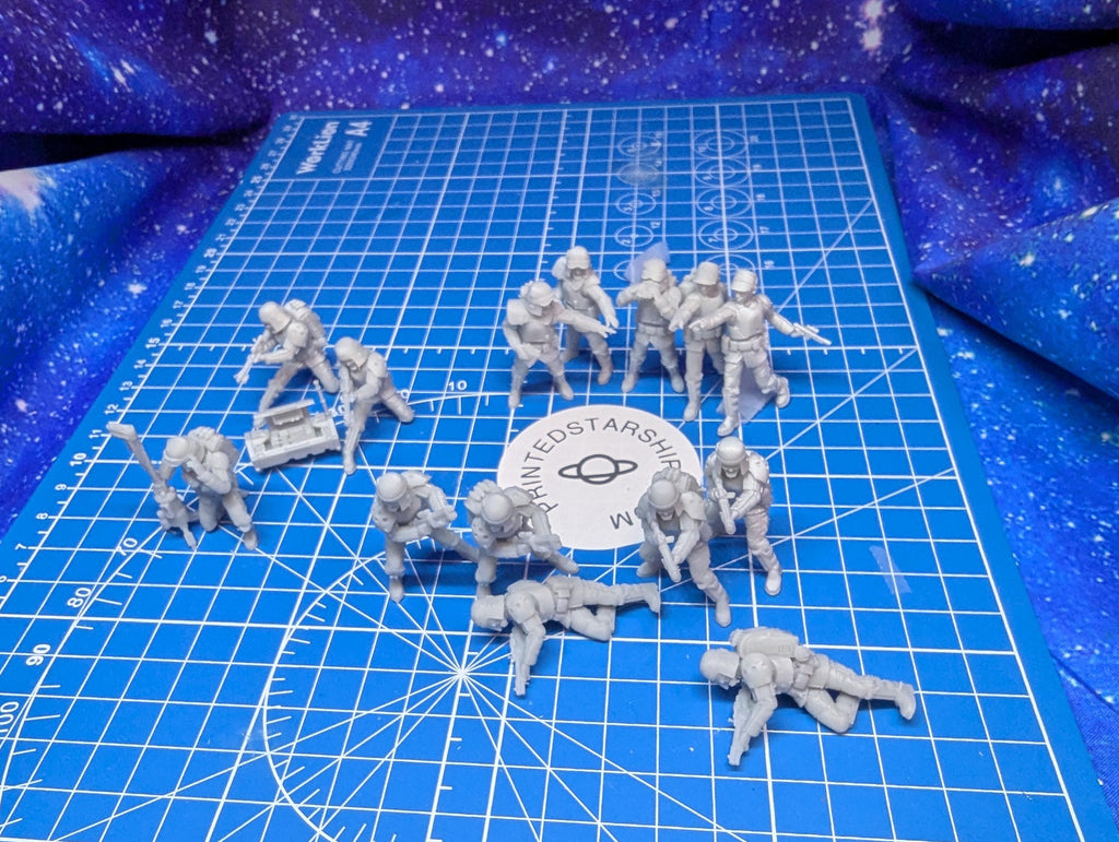 May include: A blue cutting mat with white grid lines.  There are 12 gray plastic figures of soldiers on the mat. The figures are arranged in a loose formation. The mat has the words 'PRINTED STARSHIP' in the center.